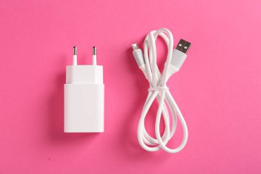 USB güç adaptörü ve pembe arka planda şarj kablosu, düz yatıyordu