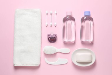 Açık pembe arka planda bebek yağı ve banyo aksesuarları.