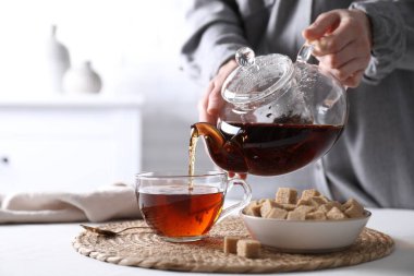 Beyaz masada fincana sıcak siyah çay dolduran kadın, yakın plan.