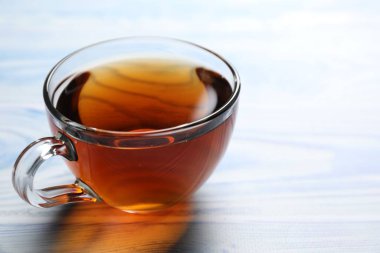 Açık mavi ahşap masada fincanda koyu siyah çay, yakın plan. Metin için boşluk