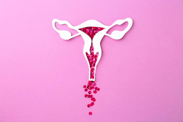 Menstruation. Paper uterus with sequins on violet background, top view