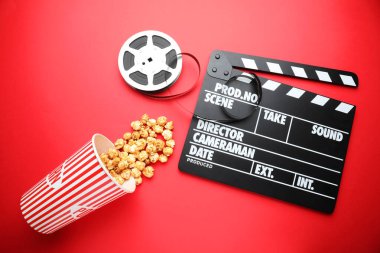 Film alkışı, tatlı patlamış mısır ve kırmızı arka planda film makarası, düz konum