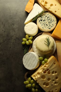 Farklı peynir türleri, biberiye ve üzümler koyu dokulu masa, düz yatak. Metin için boşluk