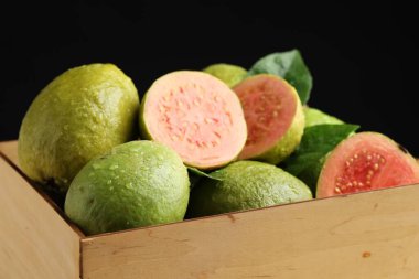 Taze kesim ve tüm guava meyveleri ahşap sandıkta siyah arka planda, yakın plan
