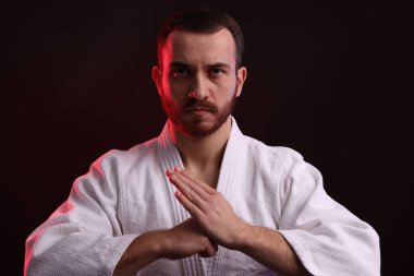 Karate dövüşçüsü siyah arkaplan karşısında renk ışığı altında üniforma giyiyor.