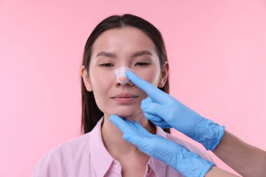 Doctor checking patient's nose after plastic surgery operation on pink background, closeup clipart