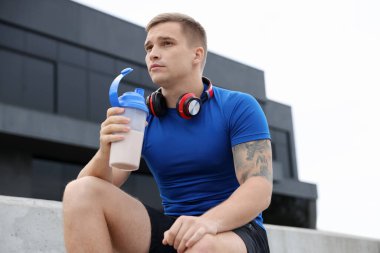 Protein salgılayan atletik bir adam açık havada içiyor, düşük açılı.