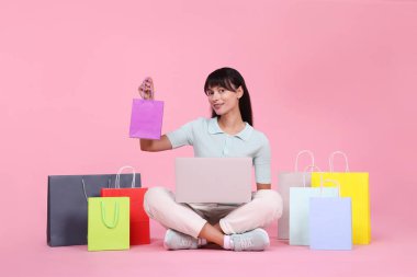 İnternet alışverişi. Dizüstü bilgisayarı ve pembe arka planda renkli çantaları olan mutlu kadın.
