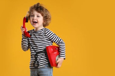 Turuncu arka planda telefonu olan sevimli küçük bir çocuk, mesaj için yeri var.