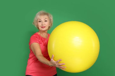 Yeşil arka planda fitness topu olan son sınıf kadın.