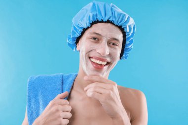 Yüzünde kremayla açık mavi arka planda duş başlığı takan bir adam.