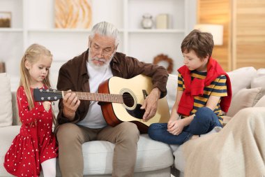 Dedem torunları için evdeki kanepede gitar çalıyor.