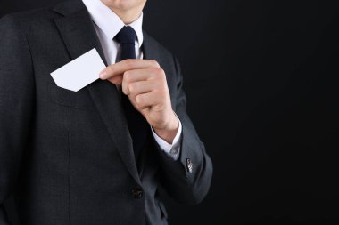 Siyah arka planda ceketinin cebinden boş kartvizit alan adam, yakın plan. Tasarım için model