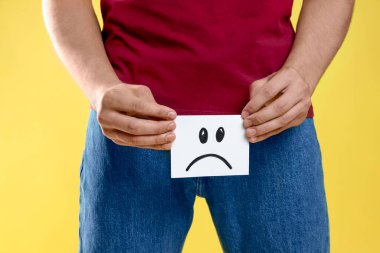 Cinsel yolla bulaşan hastalıklar. Sarı arka planda üzgün yüzü çizilmiş yapışkan bir not tutan adam, yakın plan.