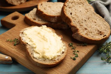 Mavi ahşap masada tereyağlı taze ekmek ve kekik, yakın plan.