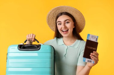 Hasır şapkalı, bavulu, bileti ve pasaportu turuncu arka planda olan bir kadın.