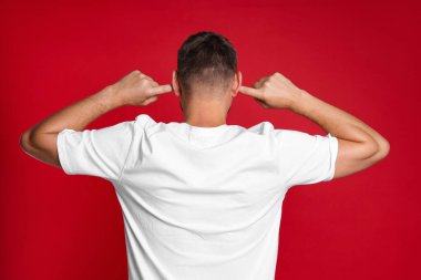 Man covering his ears with fingers on red background, back view clipart