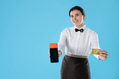 Ödeme terminali ve açık mavi arka planda kredi kartı olan mutlu garson, metin için boşluk
