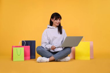 İnternet alışverişi. Laptoplu ve turuncu çantalı mutlu kadın.