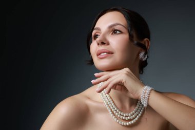 Beautiful young woman wearing elegant pearl jewelry on dark grey background clipart