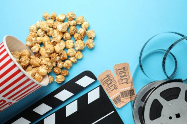 Film alkışı, tatlı patlamış mısır, biletler ve açık mavi arka planda film makarası.