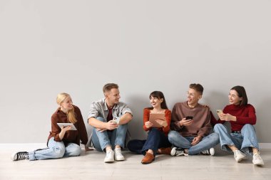 Group of people using different gadgets near light grey wall indoors. Modern technology clipart