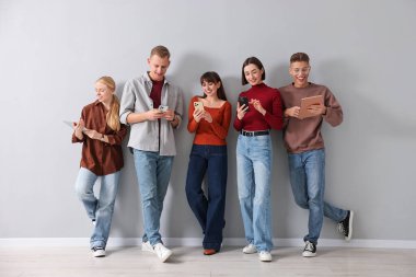 Açık gri duvarın yanında farklı aletler kullanan bir grup insan. Modern teknoloji