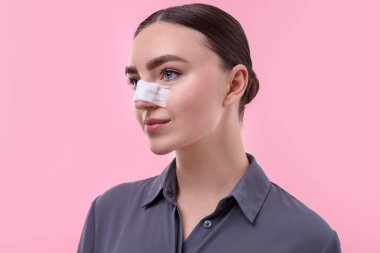 Pembe arka planda estetik ameliyat sonrası burnu bandajlı bir kadın.
