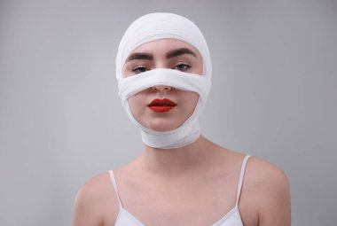 Gri arkaplandaki estetik ameliyattan sonra burnu tıbbi bandaja sarılı bir kadın.