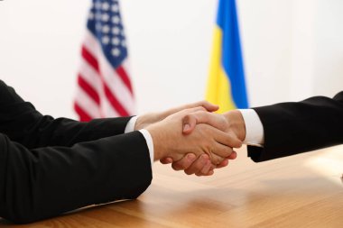 Diplomatlar ahşap masada toplanırken el sıkışıyorlar.