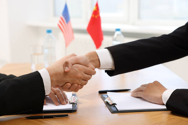 Diplomats shaking hands during meeting at wooden table indoors, closeup