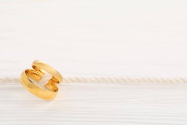 Beyaz ahşap arka planda iple bağlanmış altın alyanslar, yakın plan. Metin için boşluk