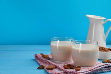 Açık mavi ahşap masa üzerinde taze fındık sütü ve badem, metin için yer