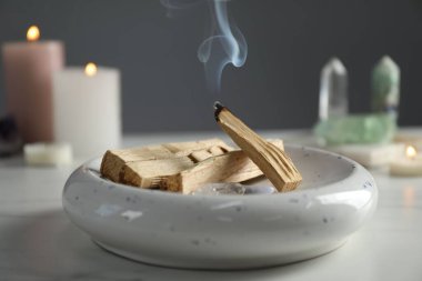 Yanan palo santo sopası, değerli taşlar ve yanan mumlar beyaz masada, yakın plan.