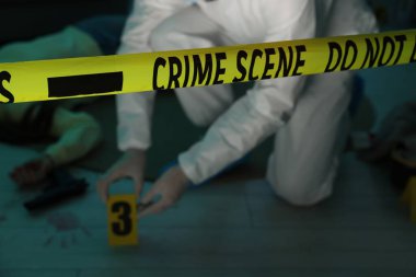 Olay yerinde çalışan adli tıp uzmanı. İçeride ölü bir kadın cesedi var. Sarı bant üzerinde yoğunlaşın.