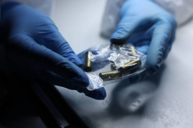 Forensic expert examining shell casings in plastic bag at table, closeup clipart