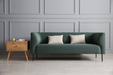 Rahat bir kanepe ve gri duvarın yanındaki yan masa.