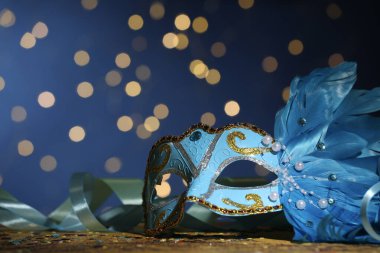 Masadaki güzel karnaval maskesi ve konfeti bulanık ışıklarla mavi arka planda.