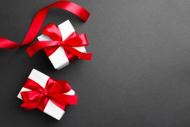 Kırmızı fiyonklu hediye kutuları ve siyah arka planda kurdele, üst manzara. Metin için boşluk