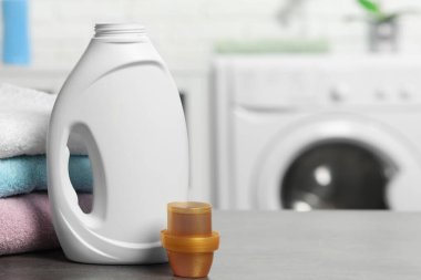 Çamaşır deterjanı, kep ve temiz havlular gri masaya istiflenmiş, metin için yer