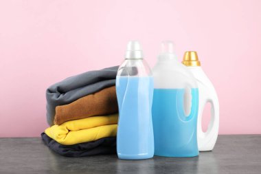 Çamaşır deterjanı şişelerde ve giysiler gri masada.