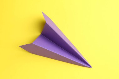 Sarı zemin üzerinde el yapımı mor kağıt uçak, üst görünüm.