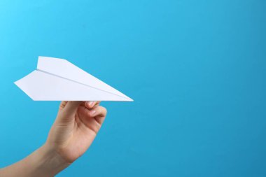 Açık mavi arka planda beyaz kağıt uçaklı kadın, yakın plan. Metin için boşluk