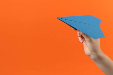 Turuncu arka planda mavi kağıttan uçağı olan kadın, yakın plan. Metin için boşluk