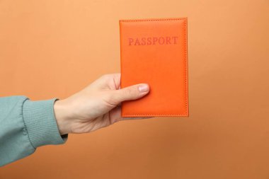 Pasaportu turuncu arka planda, parlak kapaklı bir kadın, yakın plan