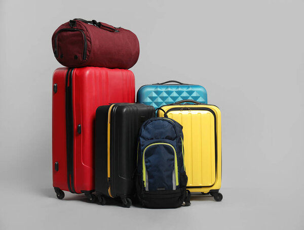 Много разноцветных чемоданов, рюкзак и сумка на сером фоне