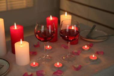 Masada kırmızı şarap, yanan mumlar ve taç yapraklarıyla romantik bir yer.
