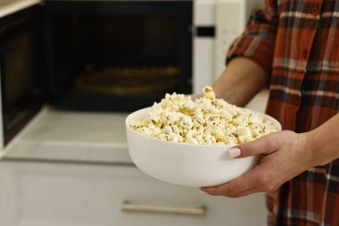 Woman with bowl of popcorn near microwave oven in kitchen, closeup. Space for text clipart