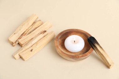 Palo Santo çubukları, yanmış bir tane ve bej arka planda yanan bir mum, yakın plan.