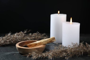 Yanmış palo santo sopası, yanan mumlar ve kurutulmuş sazlıklar karanlık masada, yakın plan.